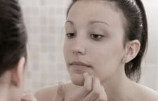 Žena sa pri pohľade do zrkadla dotýka brady